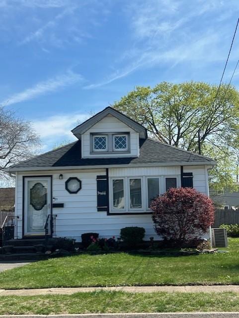 bungalow-style home with roof with shingles, fence, and a front yard