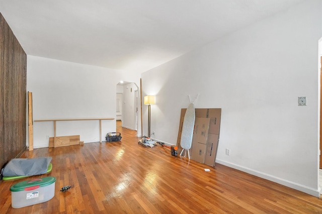 unfurnished living room featuring hardwood / wood-style flooring, arched walkways, and baseboards