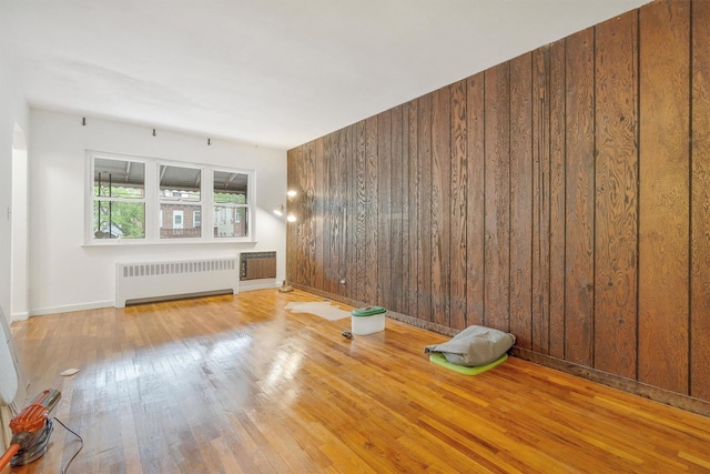 unfurnished room with wooden walls, wood finished floors, baseboards, and radiator heating unit