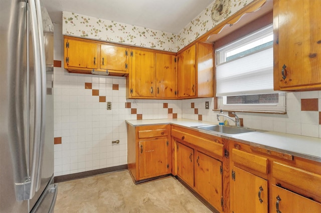kitchen featuring freestanding refrigerator, brown cabinets, light countertops, and a sink