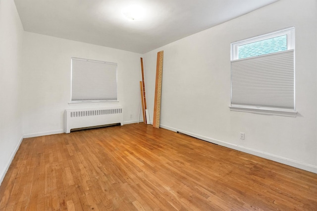 unfurnished room featuring baseboards, radiator heating unit, and light wood-style flooring