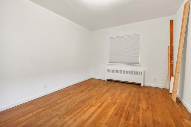 unfurnished room featuring baseboards, radiator, and light wood-style floors