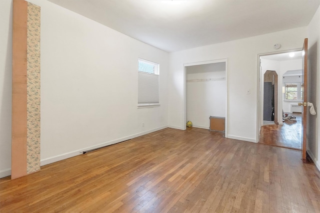 unfurnished bedroom with radiator, a closet, light wood-style floors, and baseboards