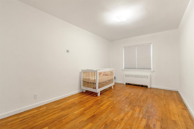 unfurnished bedroom with baseboards, light wood-style floors, and radiator heating unit