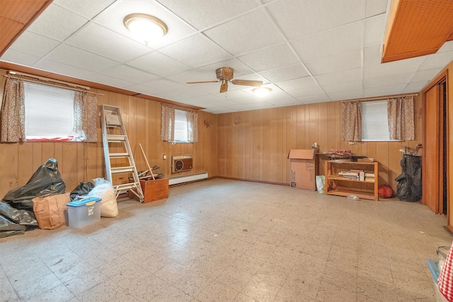 interior space with a drop ceiling, a ceiling fan, tile patterned floors, wooden walls, and a baseboard radiator