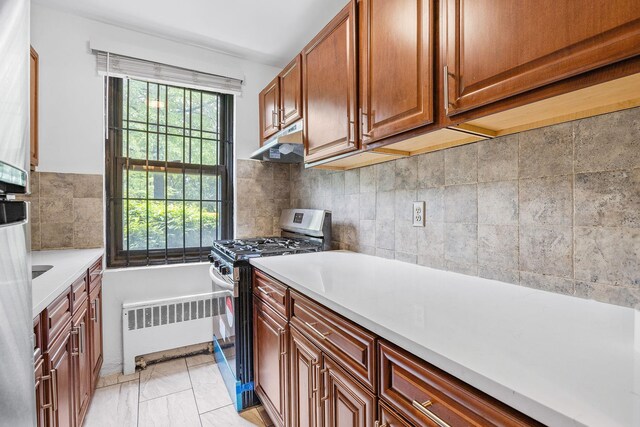 70-07 E Park Dr Unit A, Kew Garden Hills, NY 11367 - kitchen with gas range, radiator heating unit, under cabinet range hood, light countertops, and brown cabinets
