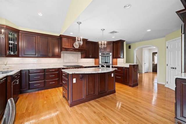 287 Old Army Rd, Scarsdale, NY 10583 - kitchen with arched walkways, a kitchen island with sink, double oven, light wood-style flooring, and recessed lighting