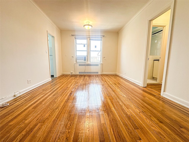 unfurnished room with crown molding, baseboards, hardwood / wood-style floors, and radiator heating unit