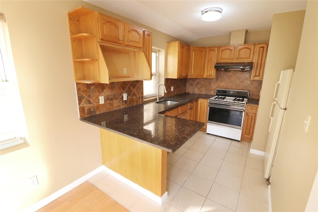 kitchen with under cabinet range hood, white appliances, a peninsula, backsplash, and dark stone counters