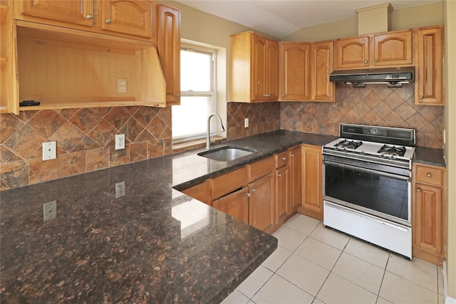 kitchen with dark stone countertops, a sink, white range with gas cooktop, under cabinet range hood, and vaulted ceiling