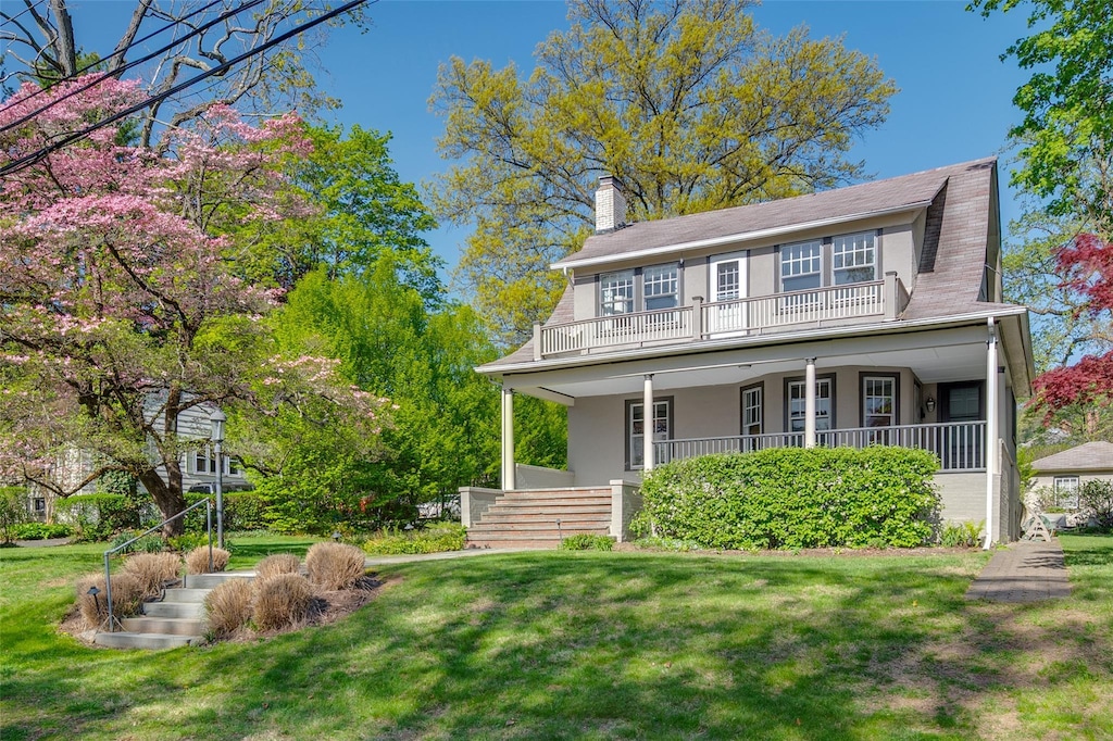 view of front of property featuring a chimney, a balcony, a front lawn, and covered porch