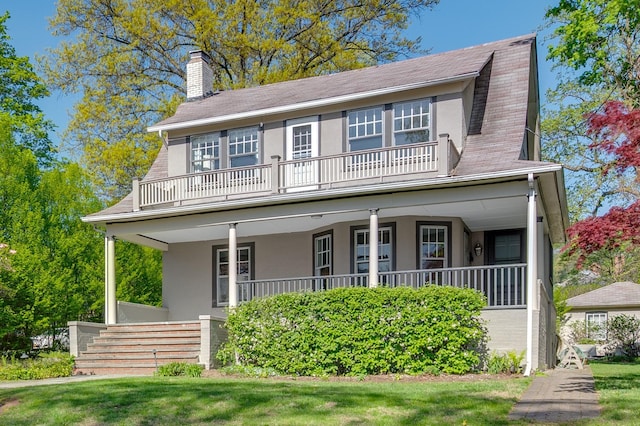 view of front facade featuring a chimney, stucco siding, a balcony, a porch, and a front lawn