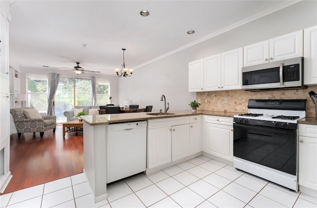 kitchen featuring stainless steel microwave, a peninsula, a sink, white dishwasher, and gas range oven