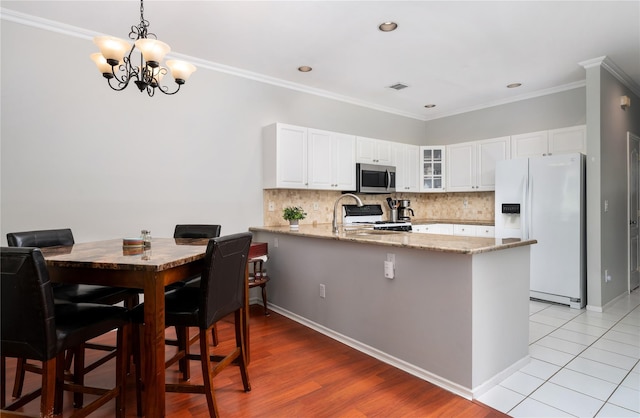 kitchen with a peninsula, white appliances, light stone counters, backsplash, and glass insert cabinets