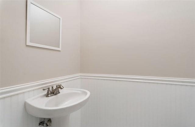bathroom featuring a decorative wall, wainscoting, and a sink