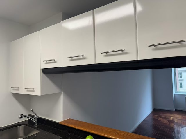 interior space with a sink, baseboards, and white cabinets