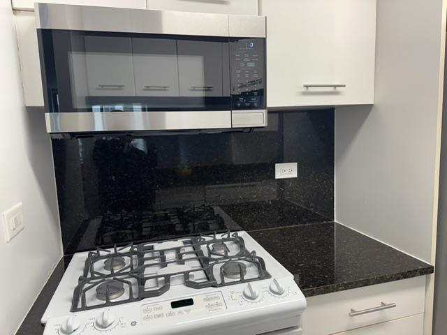 kitchen featuring stainless steel microwave, tasteful backsplash, white cabinetry, and white range with gas stovetop
