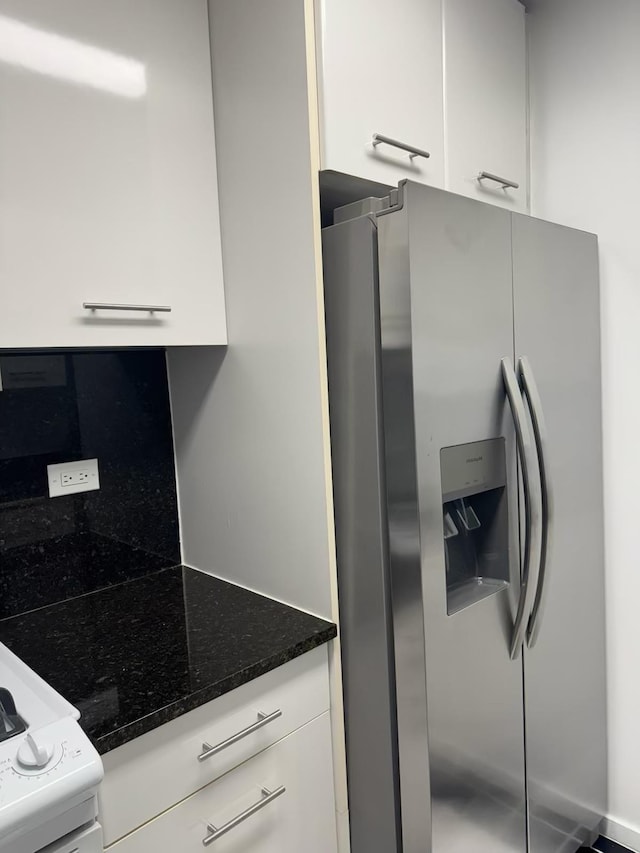 kitchen with white cabinetry, stainless steel fridge, and dark stone counters
