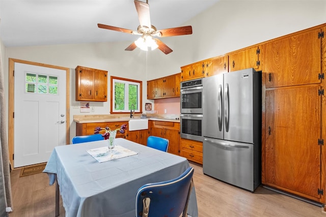 kitchen with stainless steel appliances, brown cabinetry, a ceiling fan, light wood-style flooring, and high vaulted ceiling