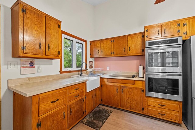 kitchen with a sink, stainless steel appliances, light wood finished floors, and brown cabinets