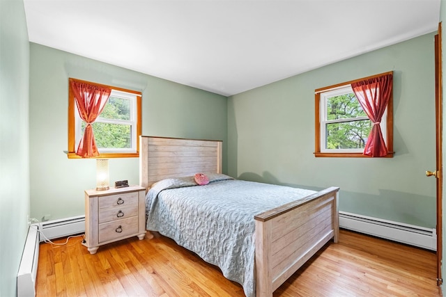 bedroom with baseboard heating, multiple windows, and light wood-type flooring