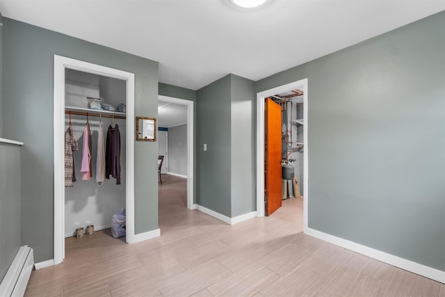 unfurnished bedroom with a baseboard heating unit, a closet, a walk in closet, and light wood-style flooring