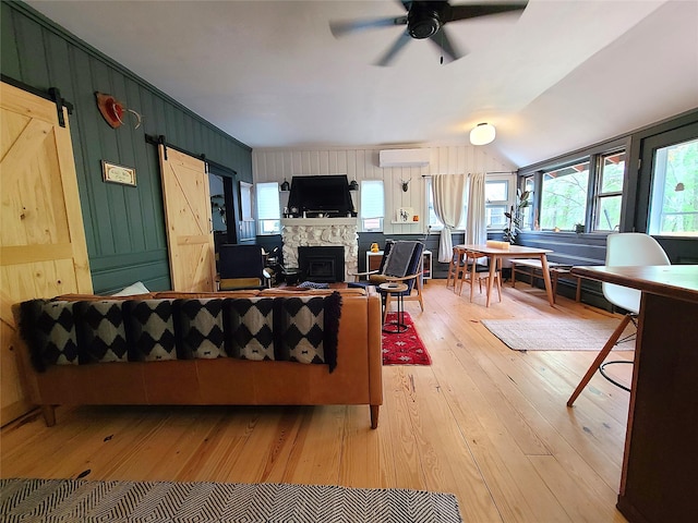 112 E Thompson Pl, Smallwood, NY 12778 - living room featuring a barn door, light wood-style flooring, a ceiling fan, a stone fireplace, and a wall mounted air conditioner