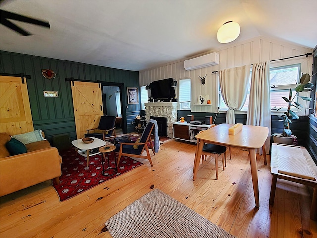112 E Thompson Pl, Smallwood, NY 12778 - living room featuring a wall mounted AC, light wood-style floors, a barn door, a stone fireplace, and lofted ceiling