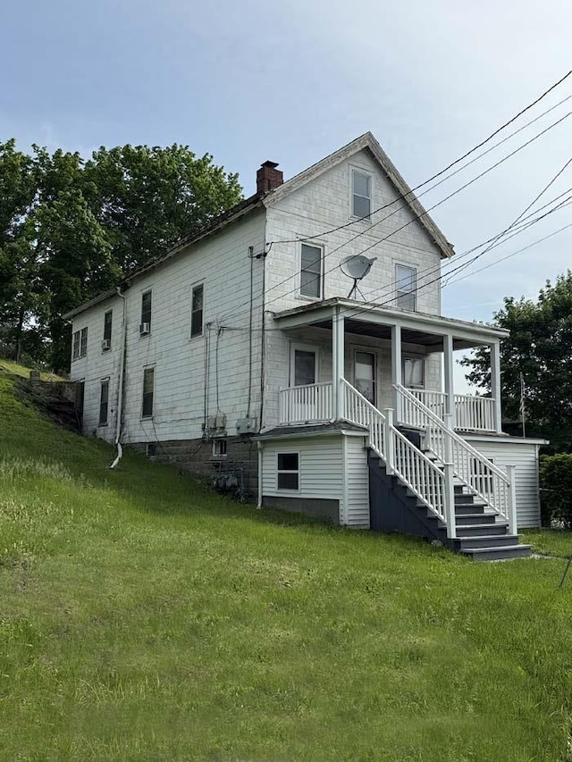 back of property with a chimney, a lawn, a porch, and stairs