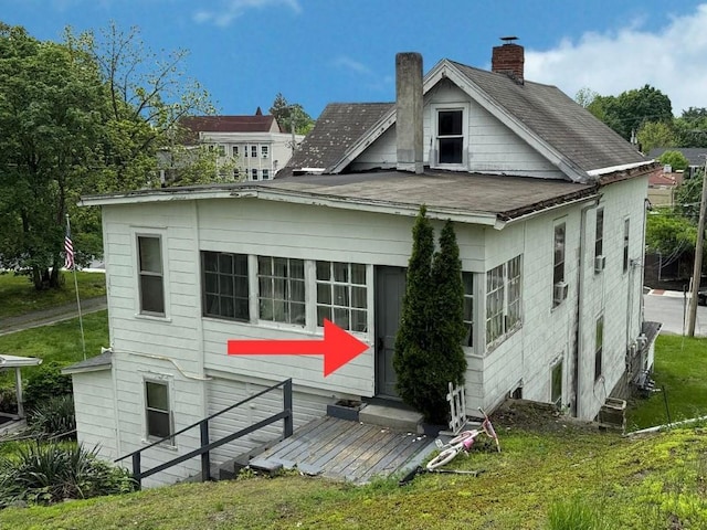 back of property with a chimney, a shingled roof, and a lawn