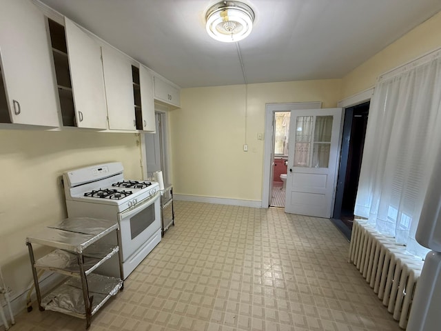 kitchen featuring white gas range oven, radiator heating unit, light floors, white cabinetry, and baseboards