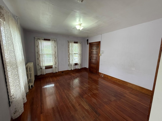 unfurnished room featuring radiator heating unit, hardwood / wood-style floors, and baseboards