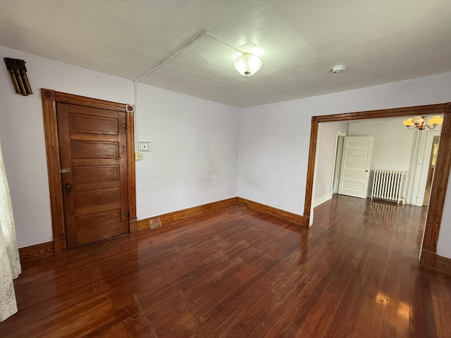 unfurnished room with radiator, hardwood / wood-style floors, a chandelier, a smoke detector, and baseboards