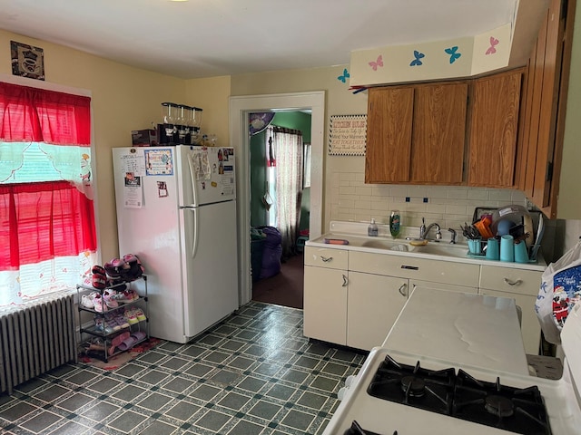 kitchen featuring freestanding refrigerator, radiator heating unit, a sink, light countertops, and dark flooring