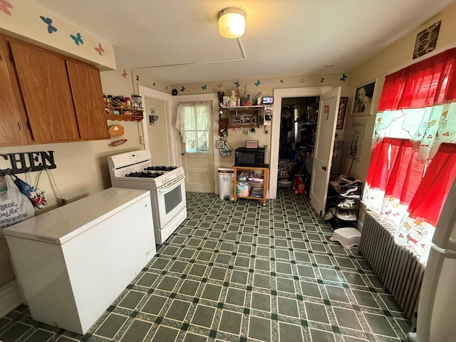 kitchen with white gas range oven, fridge, brown cabinetry, light countertops, and freestanding refrigerator