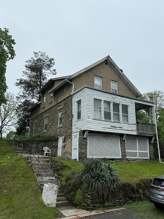 view of property exterior with a lawn, stone siding, and stairway