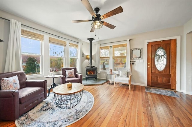 living area featuring baseboards, a wood stove, wood-type flooring, and a ceiling fan