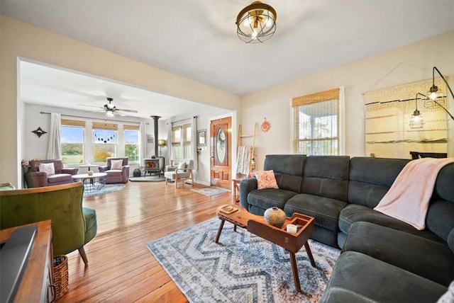 living room with a wood stove, light wood-type flooring, and a ceiling fan