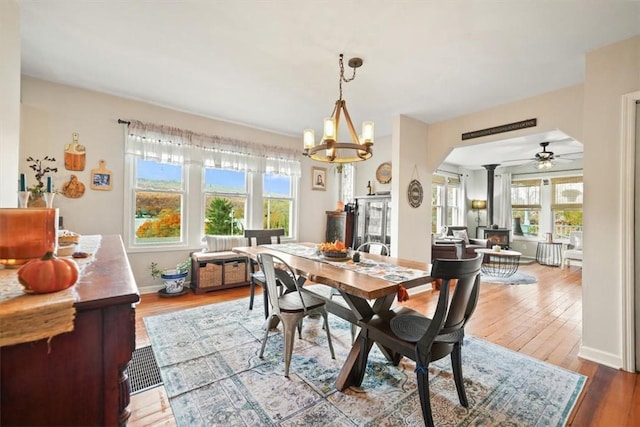 dining space with wood finished floors, ceiling fan with notable chandelier, ornate columns, baseboards, and arched walkways