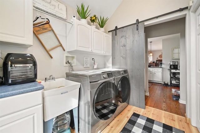 clothes washing area with a sink, cabinet space, a barn door, separate washer and dryer, and wood-type flooring