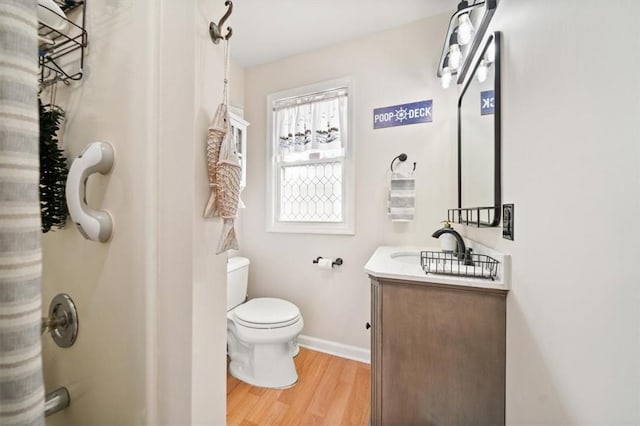 bathroom with toilet, baseboards, vanity, wood finished floors, and a shower