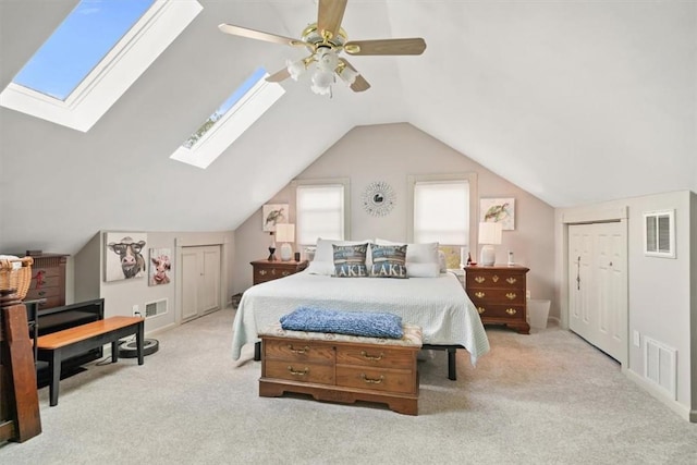 carpeted bedroom with a ceiling fan, lofted ceiling with skylight, and visible vents