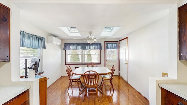 dining room featuring a skylight, light wood-type flooring, a wall mounted air conditioner, and a ceiling fan
