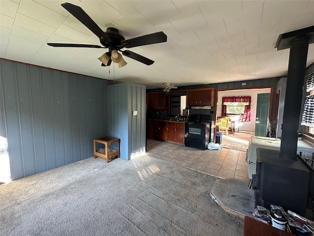 living room with a wood stove, a ceiling fan, light colored carpet, and light tile patterned floors