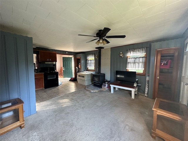 living area with a wood stove, light carpet, a ceiling fan, and wood walls