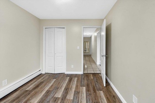 unfurnished bedroom with a closet, baseboards, wood finished floors, and a baseboard radiator