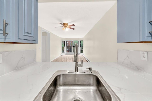 interior details with a sink, ceiling fan, decorative backsplash, and blue cabinetry