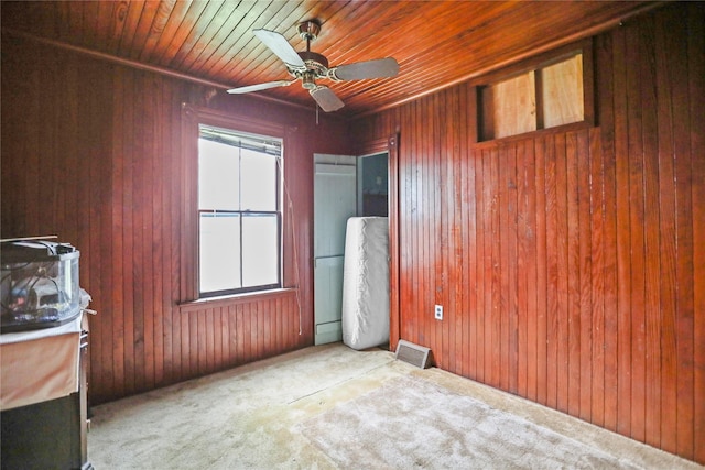 carpeted empty room with a ceiling fan, wooden walls, and wooden ceiling