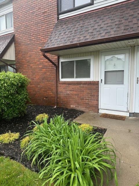 view of exterior entry with brick siding and roof with shingles