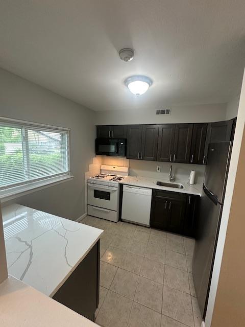 kitchen featuring a sink, white appliances, light tile patterned flooring, visible vents, and dark cabinets